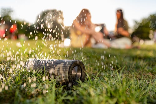 Preview: wireless waterproof speaker of friends having fun together in park listening to music