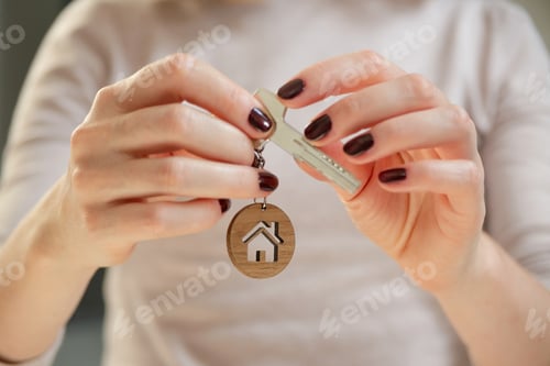 Preview: Real estate concept. Keys with a house shaped keychain in a woman's hand.