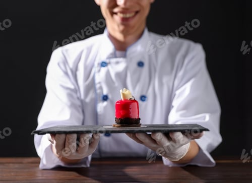 Preview: Confectioner with tasty dessert at wooden table against black background, closeup