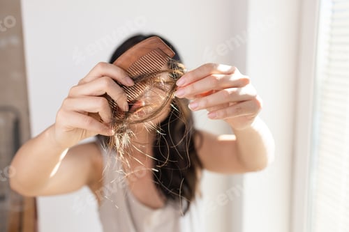 Preview: Young brunette girl holds a comb with hair falling out in her hand, looks worried and frustrated.