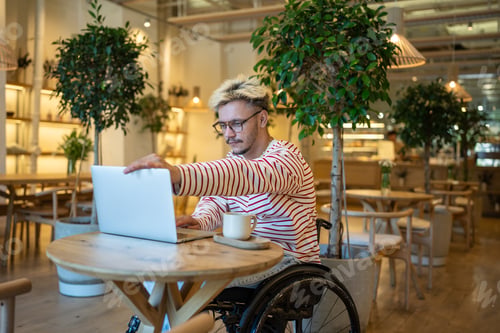 Preview: Focused diverse businessman in wheelchair opens laptop, initiates work in cafe. Work life balance