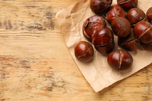 Preview: Fresh edible sweet chestnuts on wooden table, top view. Space for text