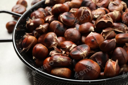 Preview: Delicious roasted edible chestnuts in frying pan on table, closeup