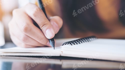 Preview: Close up image of woman's hand writing on notebook with wooden table background