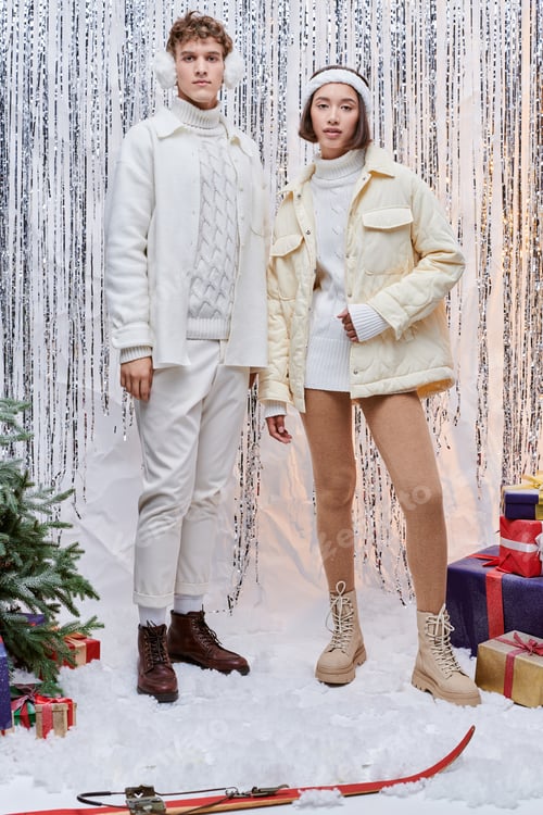 Preview: interracial models looking at camera near christmas tree and presents on silver tinsel backdrop