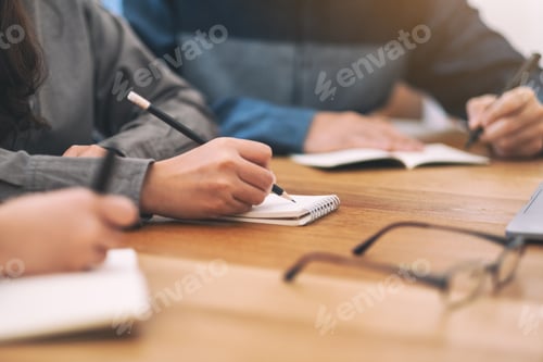 Preview: Closeup image of people writing on blank notebook together on wooden table