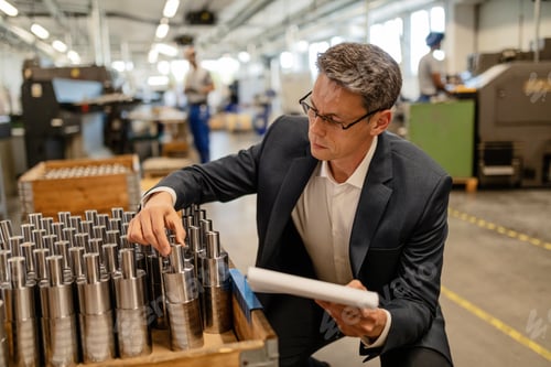 Preview: Quality control inspector examining manufactured steel cylinders in industrial building.