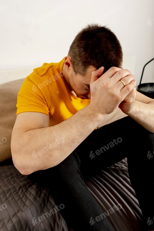 Preview: Depressed caucasian man with headache sitting alone on the bed. Stressed, lonely person