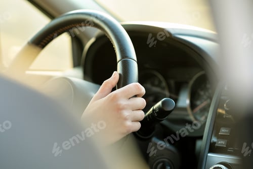 Preview: Close up view of woman hands holding steering wheel driving a car on city street on sunny day