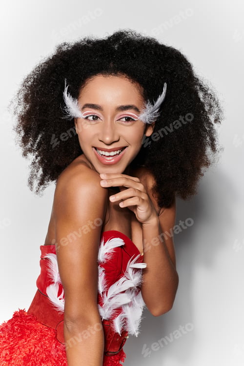 Preview: Young woman in a vibrant red outfit with feathers poses gracefully against a grey backdrop