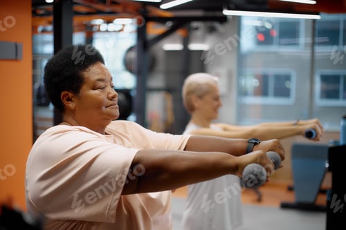 Preview: Middle Aged Black Woman Exercising with Dumbbells Beside Senior Caucasian Woman