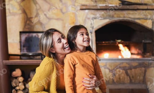 Preview: Loving mother hugging little daughter at home on patio next to the fireplace