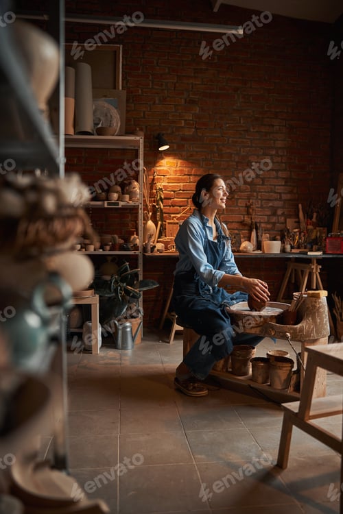 Preview: Beautiful elegant Caucasian ceramicist wearing apron shaping earthenware product in pottery workshop
