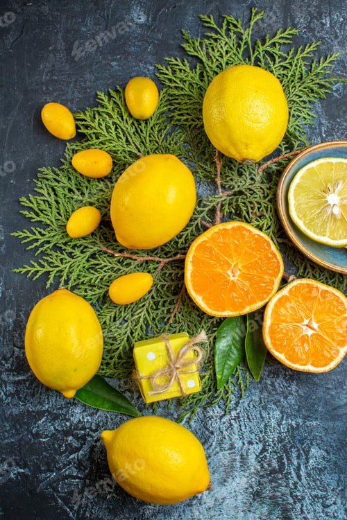 Preview: Top view of collection of half and whole citrus fruits on fir branches hand opening a gift box on