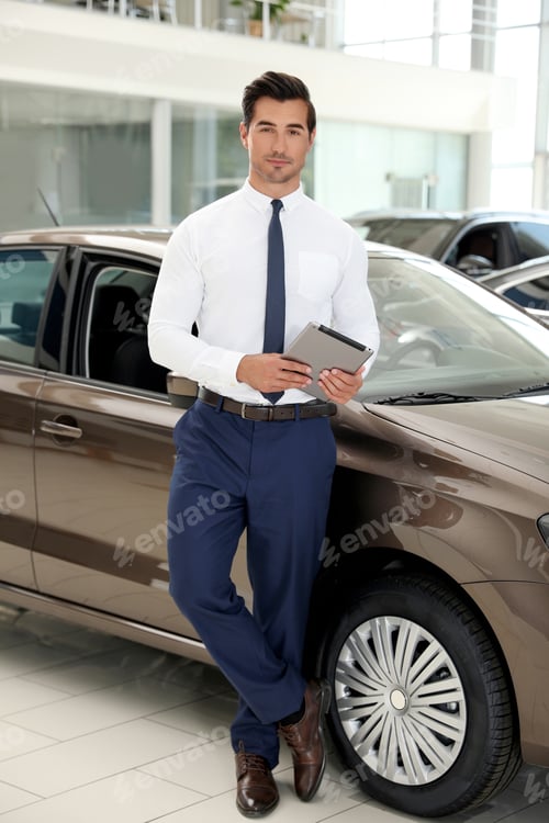 Preview: Young salesman with tablet near car in modern dealership