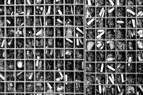 Preview: Grayscale photo of a lot of used pressed cigarettes under a square grid.