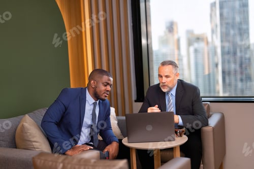 Preview: Two businessmen sitting on sofa working discuss on financial forecast together on laptop information
