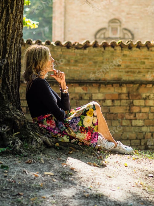 Preview: senior fit happy lady relax sit next to tree in park wear floral skirt and black long sleeve shirt