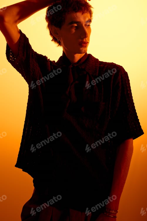 Preview: Stylish young man exudes charm against warm golden backdrop during evening glow