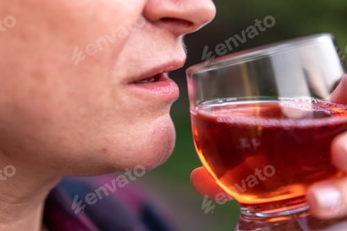 Preview: A woman drinks a red drink from a glass, close-up.