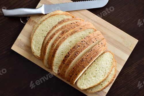 Preview: Sliced sesame bread with a knife on a bamboo chopping board. Food from above concept.