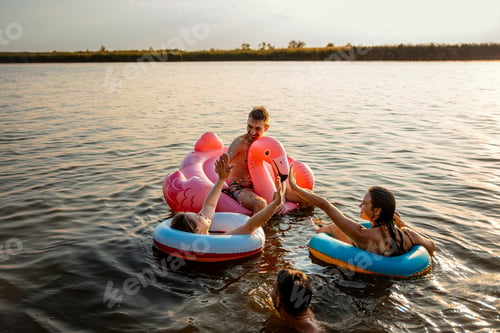 Preview: Group of young friends having fun and enjoying a summer day swimming with rubber tube at the lake.
