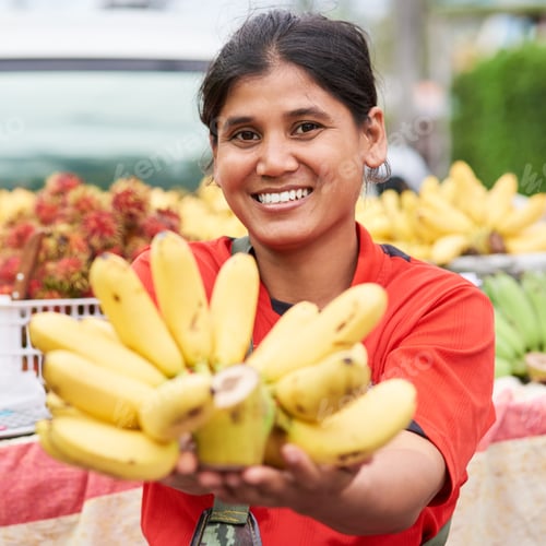 Preview: Fresh bananas. Portrait of a woman selling bananas at her market stall outside.