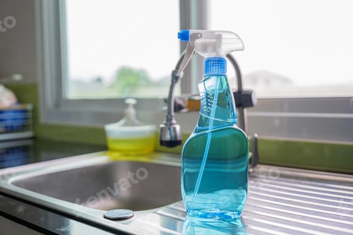Preview: Blue cleaning spray bottle placed on silver kitchen sink with a faucet in background. Represents