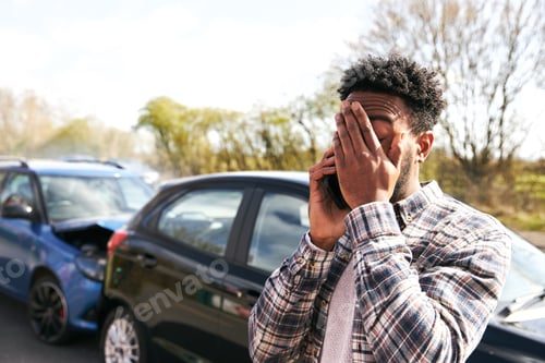 Preview: Young Male Driver Calling Car Insurance Company On Mobile Phone After Road Traffic Accident