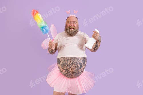 Preview: Happy man with overweight in fairy costume holds duster and detergent on purple background