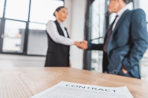 Preview: close-up view of contract on table and business people shaking hands behind