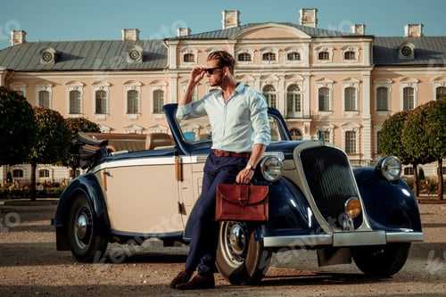 Preview: Confident wealthy young man with briefcase near classic convertible