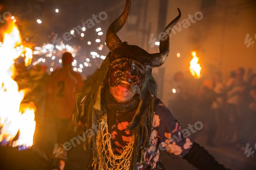 Preview: Person in a horned mask amidst a fiery celebration