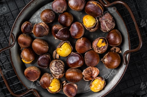 Preview: Cracked roast chestnuts served in a tray. Black background. Top view