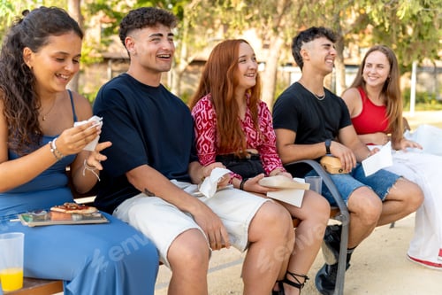 Preview: Young people enjoying take away food on a bench in a park