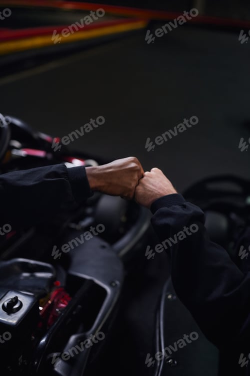 Preview: cropped view of diverse go kart drivers fist bumping and sitting in sport cars for karting