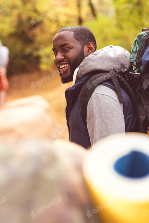 Preview: Young smiling man backpacker talking with blurred male friend on foreground