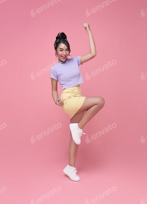 Preview: Happy Asian woman smiling and jumping while celebrating success isolated over pink background.