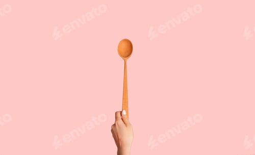 Preview: Millennial woman holding wooden spoon over pink background, close up