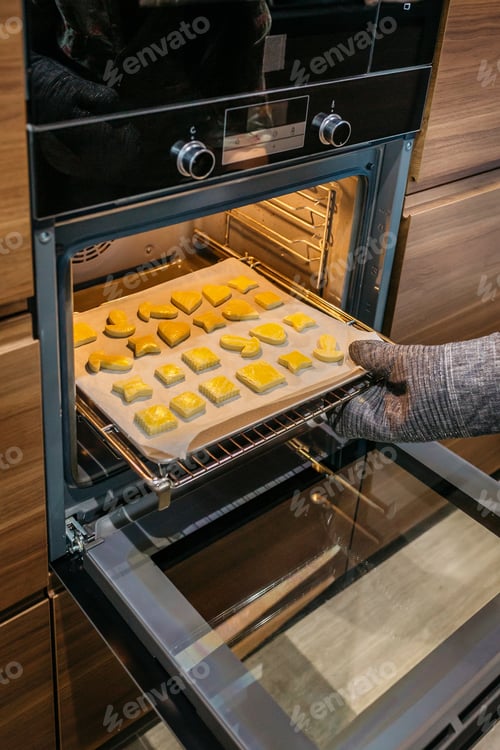 Preview: Unrecognizable hand taking a baking pan full of golden cookies out of the oven in the kitchen