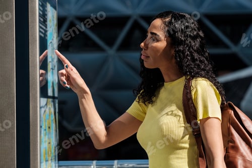 Preview: Young woman pointing at display map outdoors.