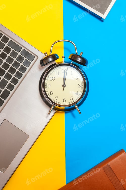 Preview: Concept time to work. Alarm clock with a laptop and books on a yellow and blue background.
