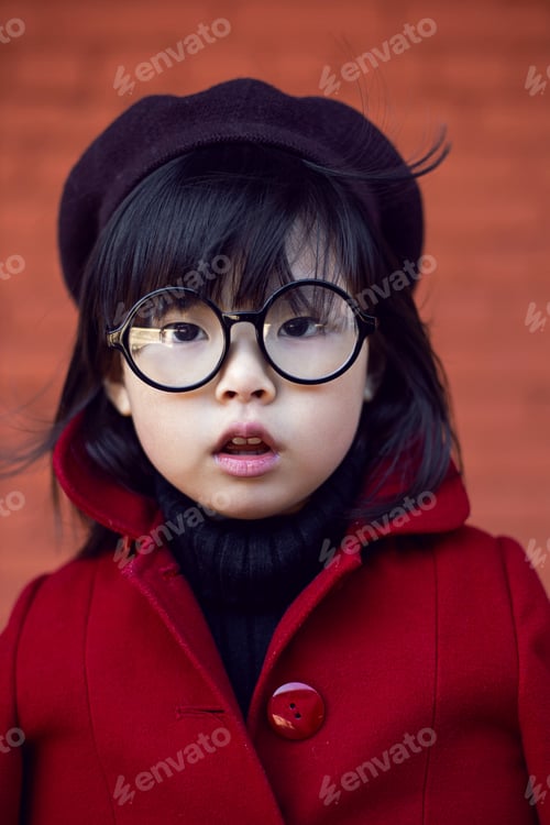 Preview: Korean girl in a red coat and cap and round glasses stands on red brick wall the street in autumn.