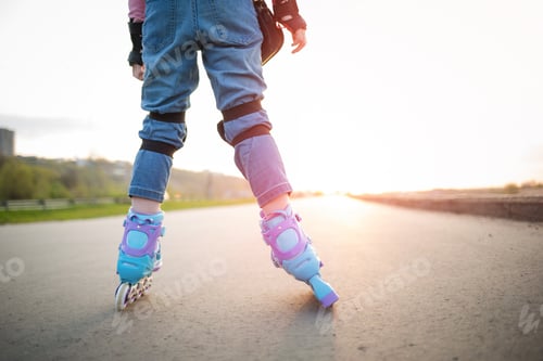 Preview: child on roller skates on background of road in rays of sunset