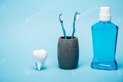 Preview: Toothbrushes, tooth model and bottle of mouthwash on blue background