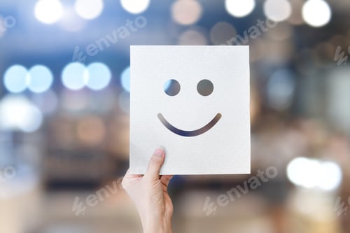 Preview: Hand holding white paper with smiley face emoticons (perforated paper) over light bokeh background.