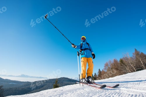 Preview: Male skier using selfie stick taking photos while skiing