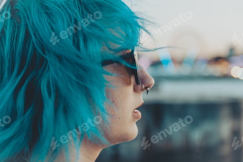Preview: Portrait of a young female with blue and pink hair wearing sunglasses with a blurred background