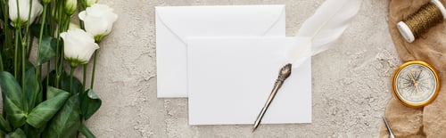 Preview: panoramic shot of quill pen on empty card, eustoma flowers, compass and spool on beige sackcloth on