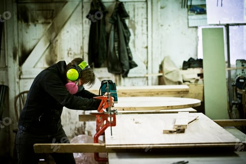 Preview: A woman working in a furniture maker's workshop cutting timber with a saw.